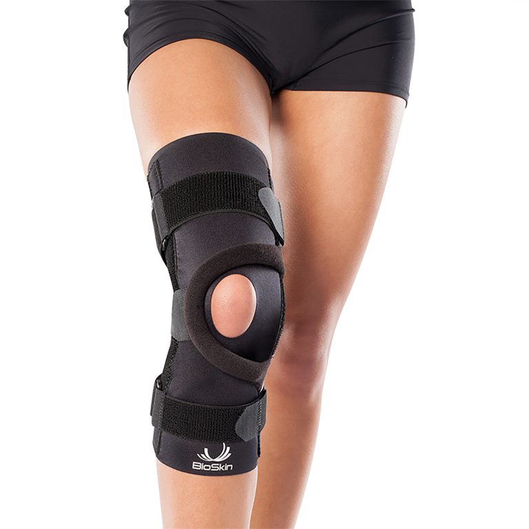 BioSkin Q Brace pull-on knee support worn on a leg, showing the open-patella design and adjustable T-strap for kneecap tracking.